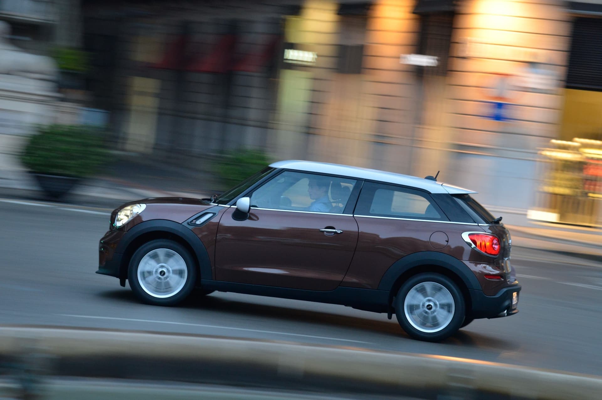 MINI Cooper S Paceman w kolorze brązowym z białym dachem w ruchu przez miejską ulicę